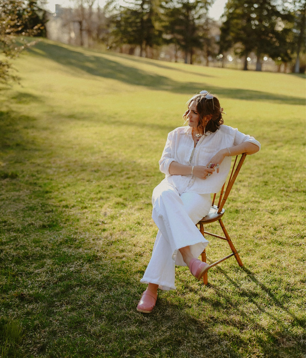 Woman in a white dress sitting on a wooden chair in a grassy field