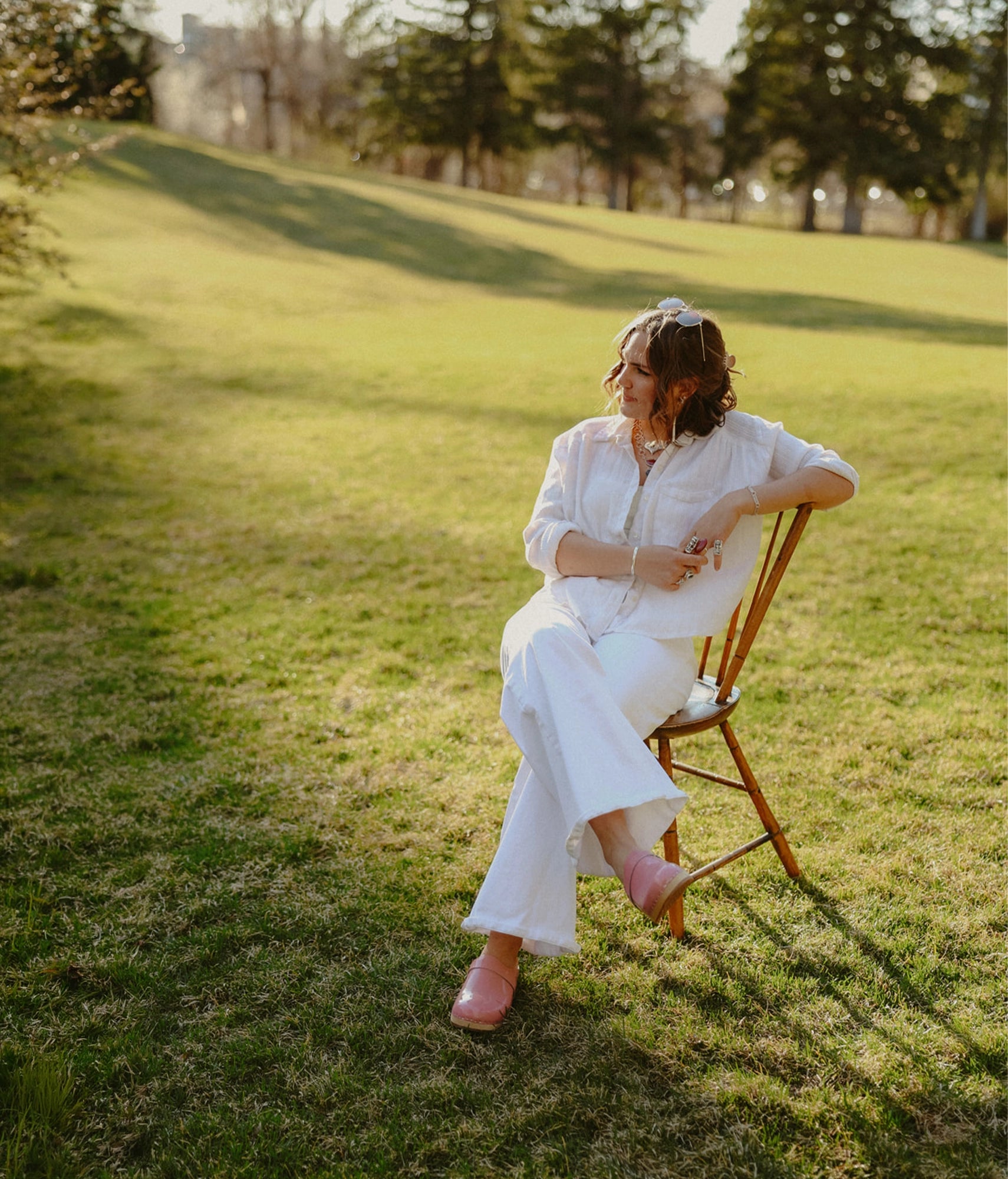 Woman in a white dress sitting on a wooden chair in a grassy field