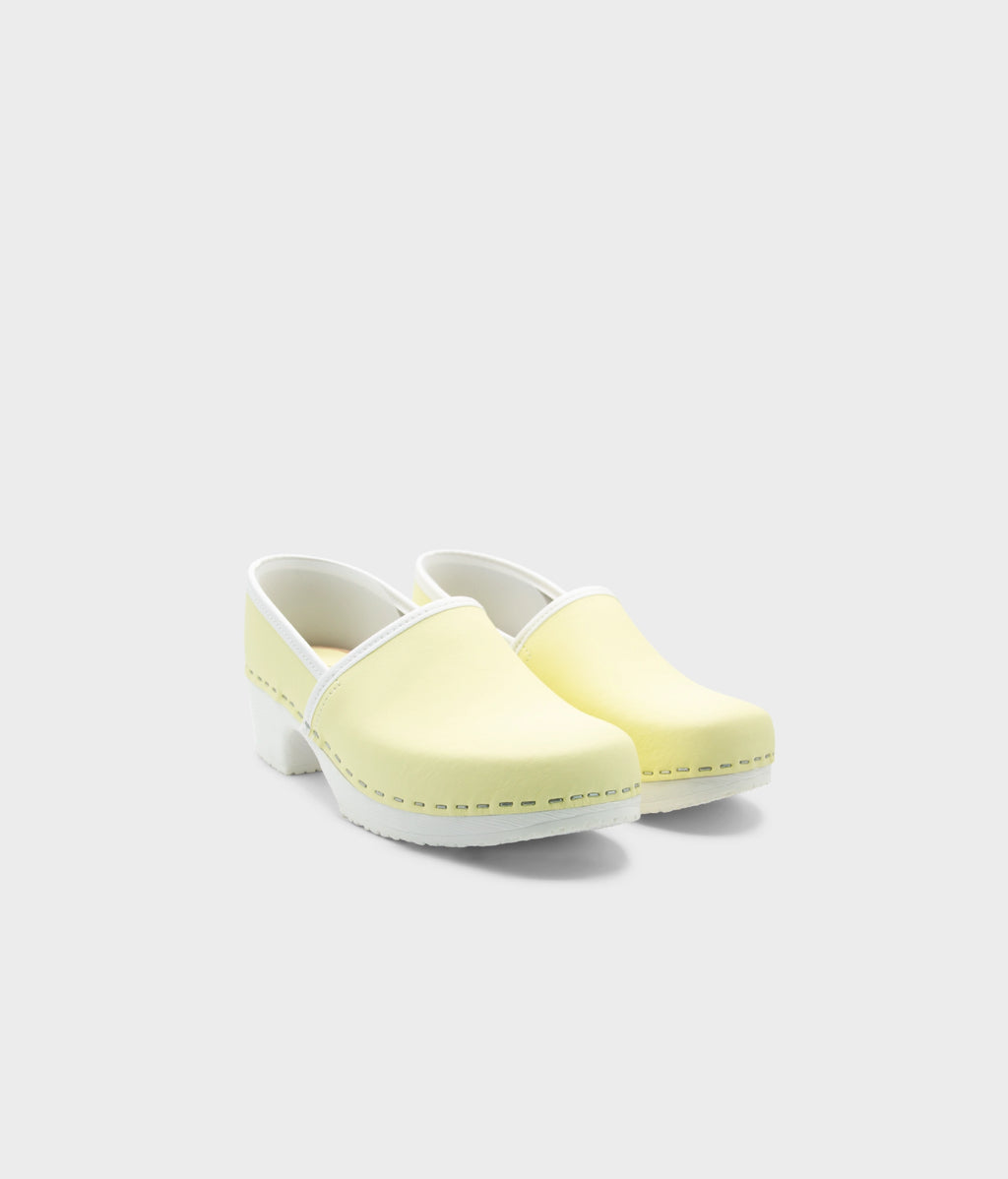 Pair of light yellow clogs with white soles on a white background