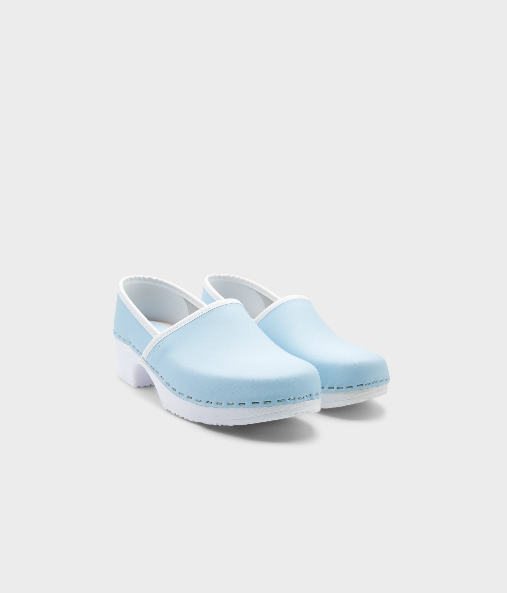 Pair of light blue clogs with white soles on a white background